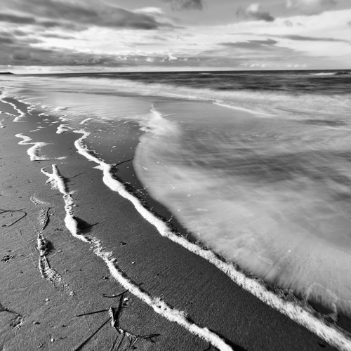 Schwarzweiß-Aufnahme der Ostsee. Meeressaum mit Schaum vor dem verwaschenen Meer.