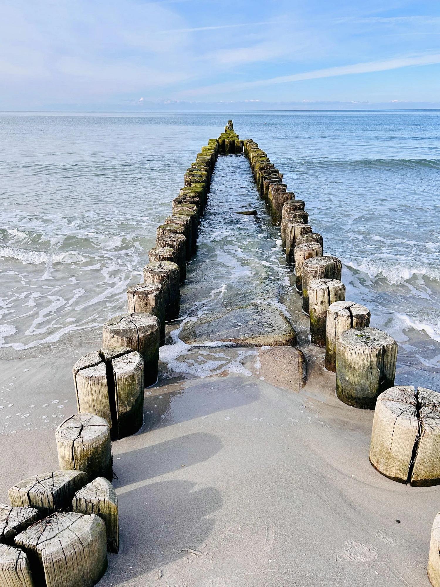 Frontaler Blick auf eine zweigeteilte Buhne, die in die Ostsee ragt.