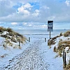 Blick auf die Ostsee durch einen Strandzugang. Es liegt leichter Schnee, der Himmel ist wolkenverhangen.