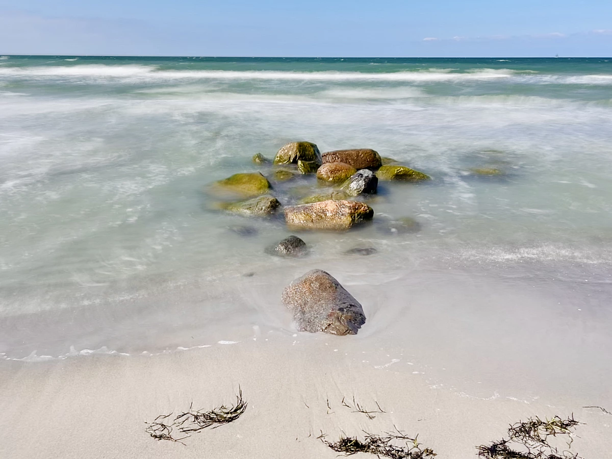 Im Mittelpunkt liegen mehrere große Steinen am Strand und in der Ostsee. Das Wasser drumherum ist durch Langzeitbelichtung verwaschen.