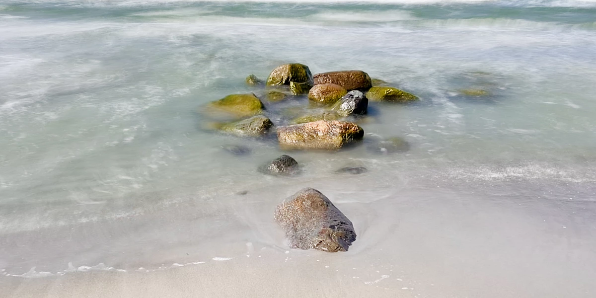 Im Mittelpunkt liegen mehrere große Steinen am Strand und in der Ostsee. Das Wasser drumherum ist durch Langzeitbelichtung verwaschen.