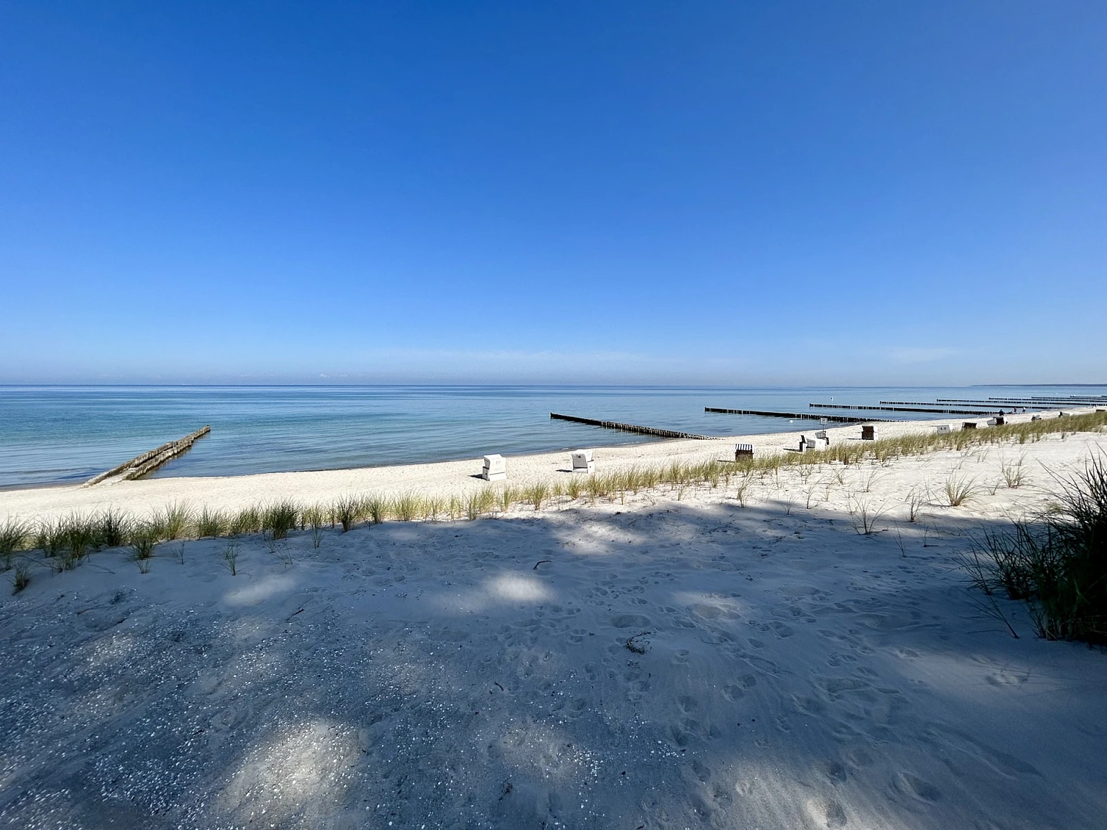 Blick auf das stille Meer mit Buhnen, im Vordergrund Sandstrand