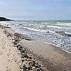 Diagonal geteilt links der nasse Strand, rechts das stürmische Meer mit blauem Himmel.