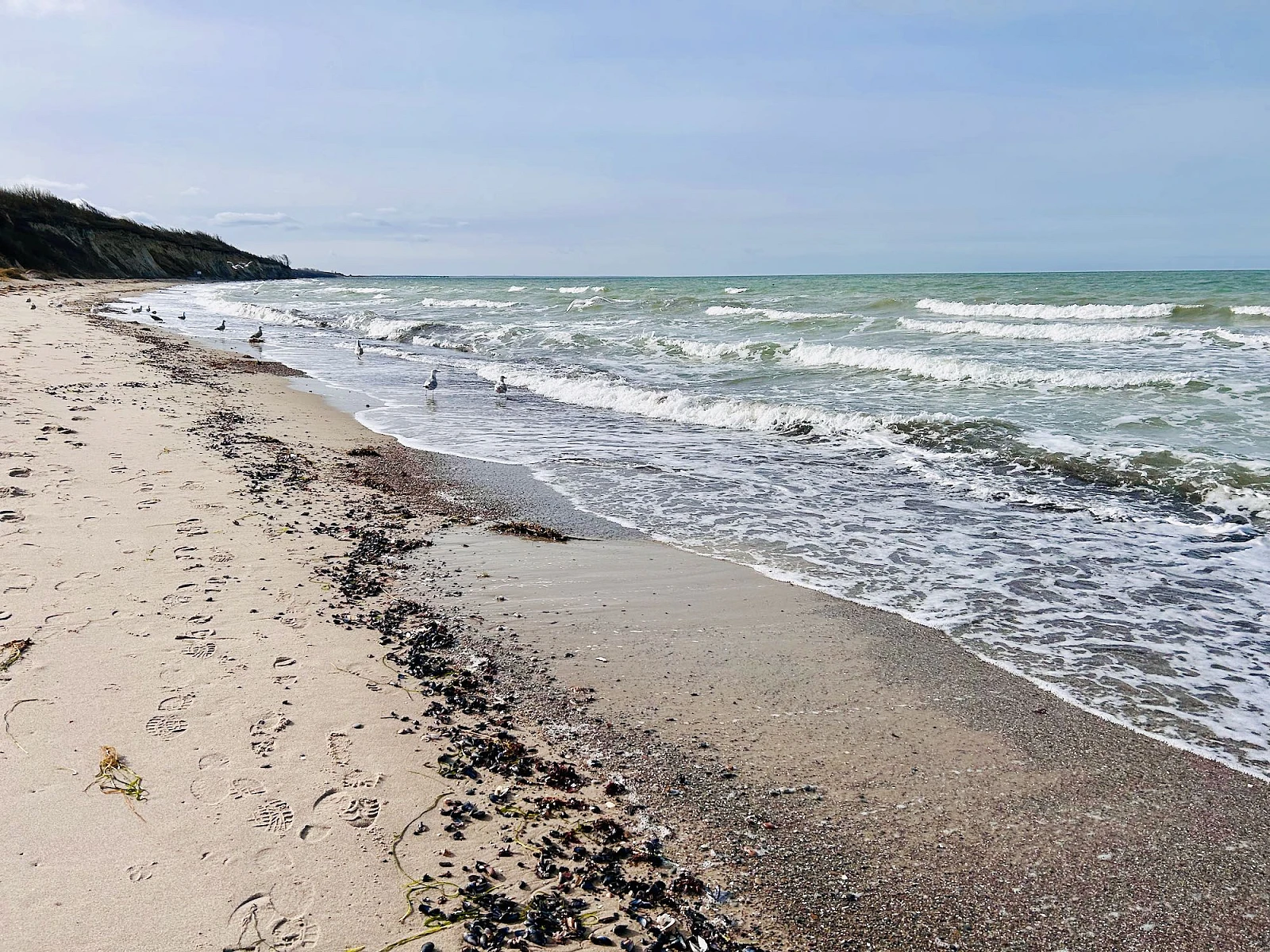 Diagonal geteilt links der nasse Strand, rechts das stürmische Meer mit blauem Himmel.