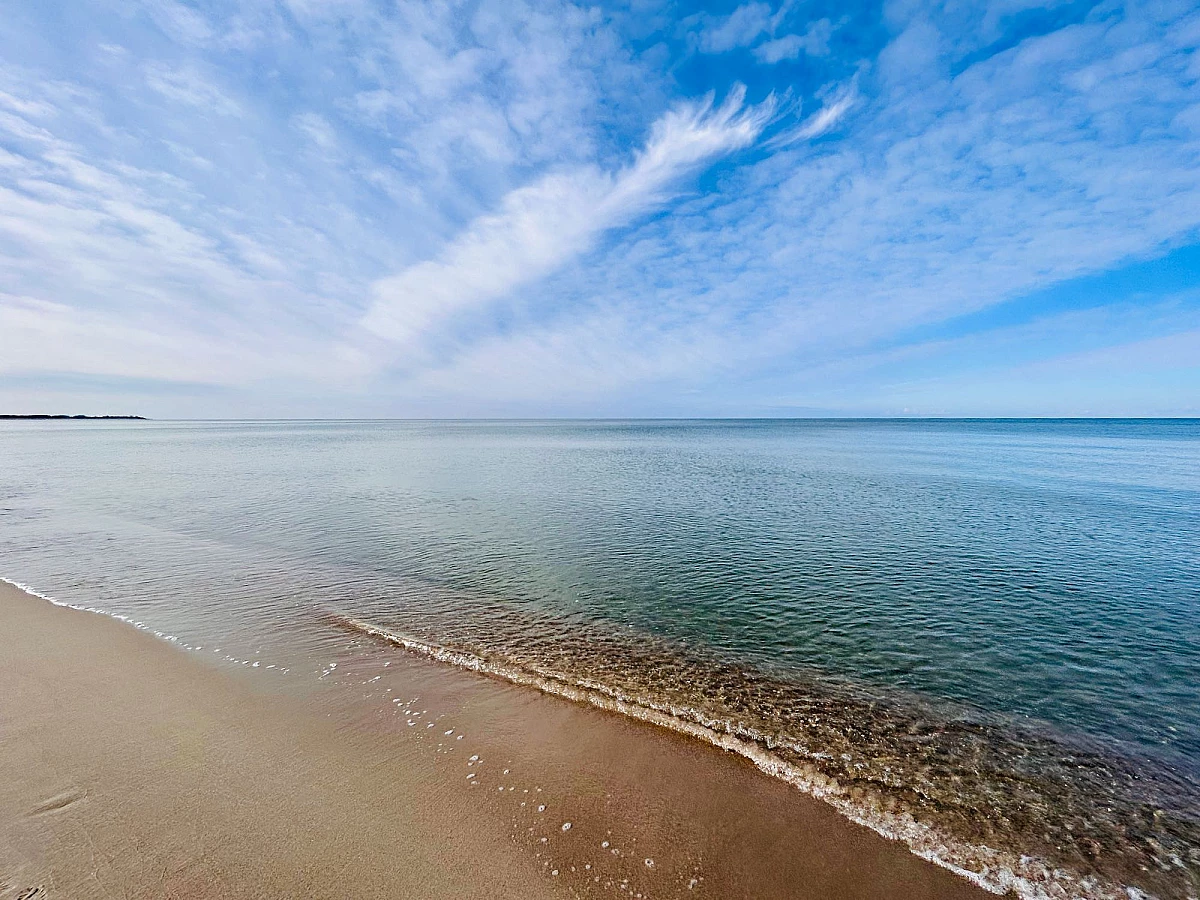 Blick auf die ruhige Ostsee, die ebenso wie der Himmel blau ist. Leichte Schleierwolken ziehen zum Horizont.