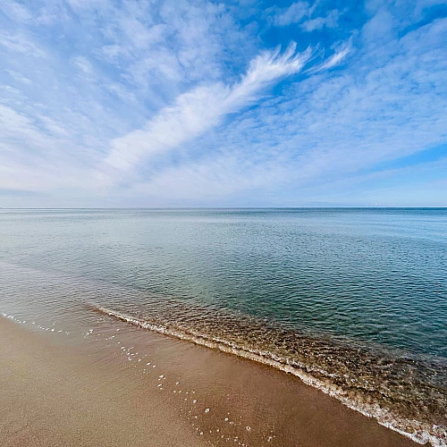 Blick auf die ruhige Ostsee, die ebenso wie der Himmel blau ist. Leichte Schleierwolken ziehen zum Horizont.