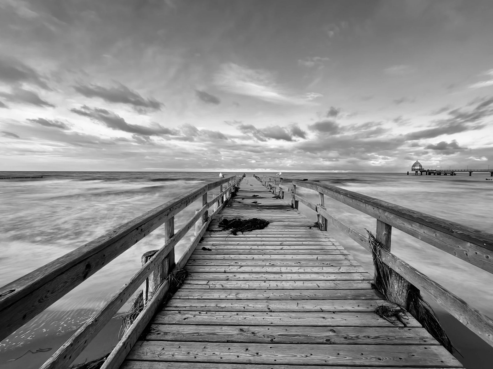 Schwarzweiß-Aufnahme der Ostsee. Blick auf einen langen Holzsteg.