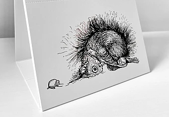 Der Kalender steht aufgeklappt auf einer weißen Fläche. Es ist der Monat Februar zu sehen. Es ist eine Illustration zu sehen, auf der ein Eichhörnchen und zwei Haselnüsse in der Kindspose verweilen.