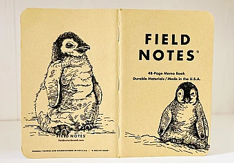 Foto eines aufgeklappten Field Notes Heftes mit Kraft-Papier-Deckel. Auf Rücken und Cover befindet sich jeweils eine schwarze Zeichnung eines sitzenden Baby Pinguins.
