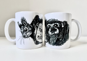 Zwei weiße Keramiktassen stehen nebeneinander. Auf der linken Tasse die schwarze Zeichnung eines Eichhörnchenkopfes, auf der rechten die schwarze Zeichnung eines Faultiers.