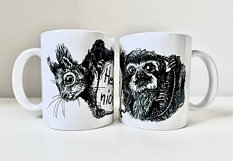 Zwei weiße Keramiktassen stehen nebeneinander. Auf der linken Tasse die schwarze Zeichnung eines Eichhörnchenkopfes, auf der rechten die schwarze Zeichnung eines Faultiers.