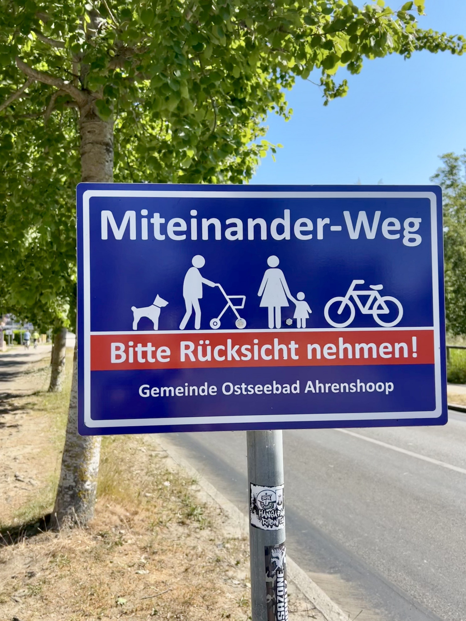 Foto eines Schildes auf dem ein Hund, ein Mensch mit Rollator, eine Person mit Kind und ein Fahrrad zu sehen sind. Aufschrift: 
Miteinander-Weg
Bitte Rücksicht nehmen!
Gemeinde Ostseebad Ahrenshoop