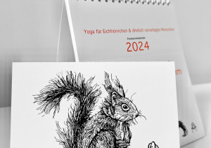 Der Kalender "Ommmmmmmmmmmm - Yoga für Eichhörnchen & ähnlich veranlagte Menschen - Postkartenkalender 2024" steht aufgeklappt auf einer weißen Fläche. Im Vordergrund eine abgetrennte Postkarte.