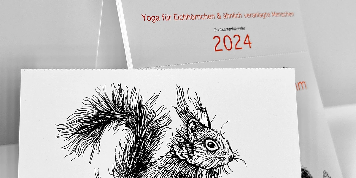 Der Kalender "Ommmmmmmmmmmm - Yoga für Eichhörnchen & ähnlich veranlagte Menschen - Postkartenkalender 2024"  steht aufgeklappt auf einer weißen Fläche. Im Vordergrund eine abgetrennte Postkarte.