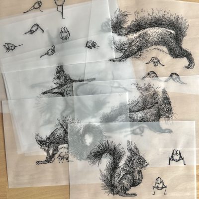 Viele Blätter Transparentpapier mit Tintezeichnungen liegen übereinander auf einem Holztisch.