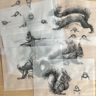 Viele Blätter Transparentpapier mit Tintezeichnungen liegen übereinander auf einem Holztisch.