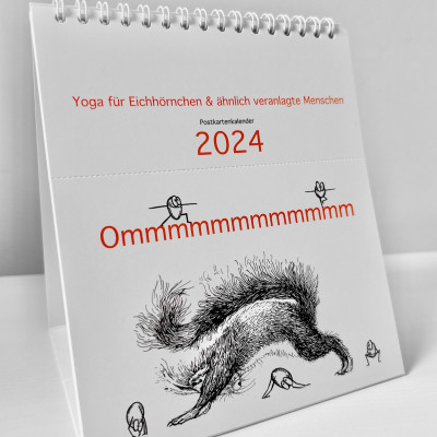 Der Kalender Ommmmmmmmmmmm - Yoga für Eichhörnchen & ähnlich veranlagte Menschen - Postkartenkalender 2024  steht seitlich aufgeklappt auf einer weißen Fläche. Auf dem Cover ist ein Eichhörnchen zu sehen, das die Position des herabschauenden Hundes praktiziert.  Fünf Haselnüsse praktizieren ebenfalls Yoga.