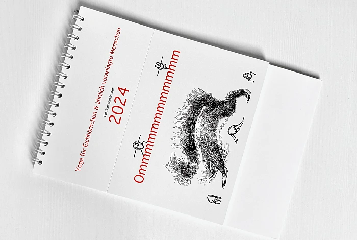 Der Kalender Ommmmmmmmmmmm  liegt flach und diagonal auf einer weißen Fläche. Auf dem Cover ist ein Eichhörnchen zu sehen, das die Position des herabschauenden Hundes praktiziert.  Fünf Haselnüsse praktizieren ebenfalls Yoga.