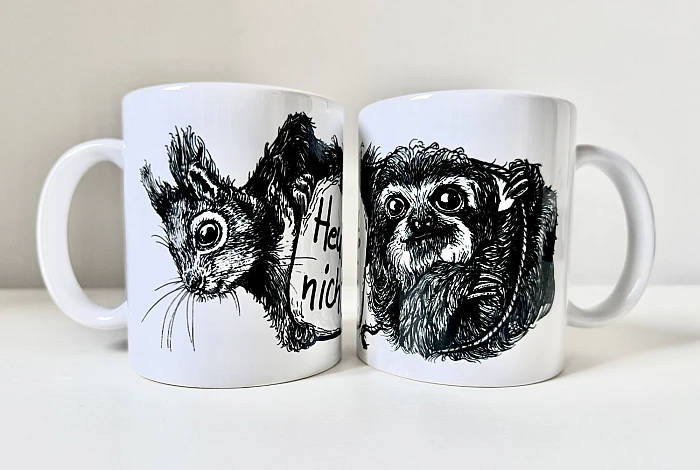 Zwei weiße Keramiktassen stehen nebeneinander. Auf der linken Tasse die schwarze Zeichnung eines Eichhörnchenkopfes, auf der rechten die schwarze Zeichnung eines Faultiers.